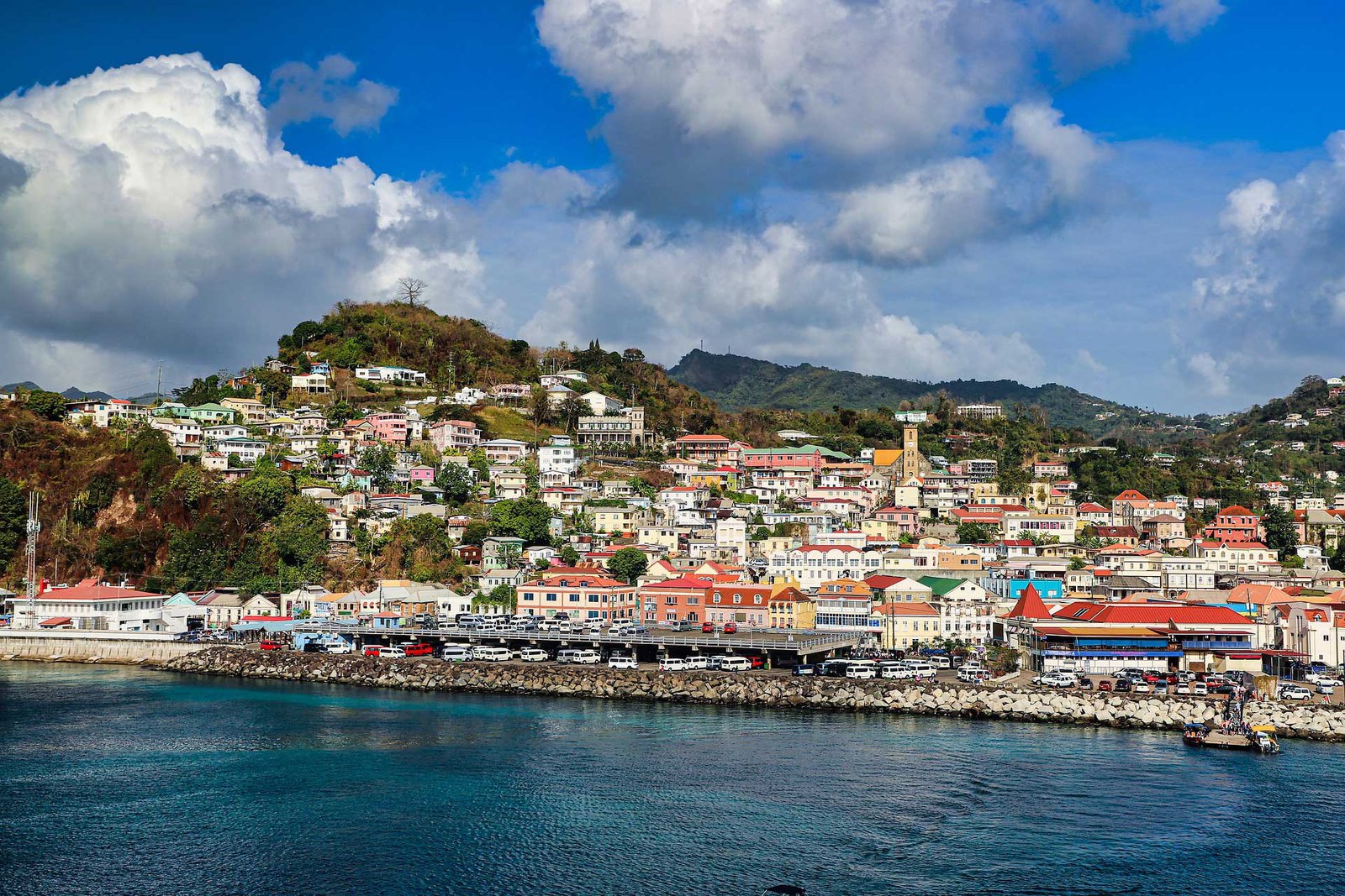 A city on the coast of Grenada with a harbor and mountains in the background