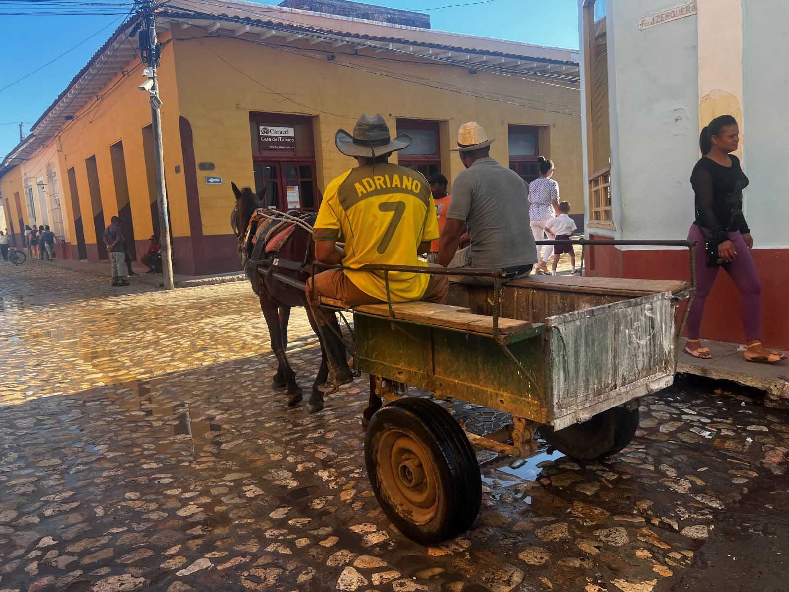 A man riding a horse pulling a cart down a cobblestone street in Trinidad