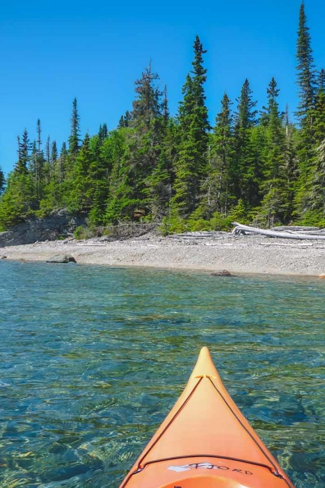 A first-person view from a kayak on the clear, calm waters of Lake Superior, showcasing one of the best things to do in the Upper Peninsula