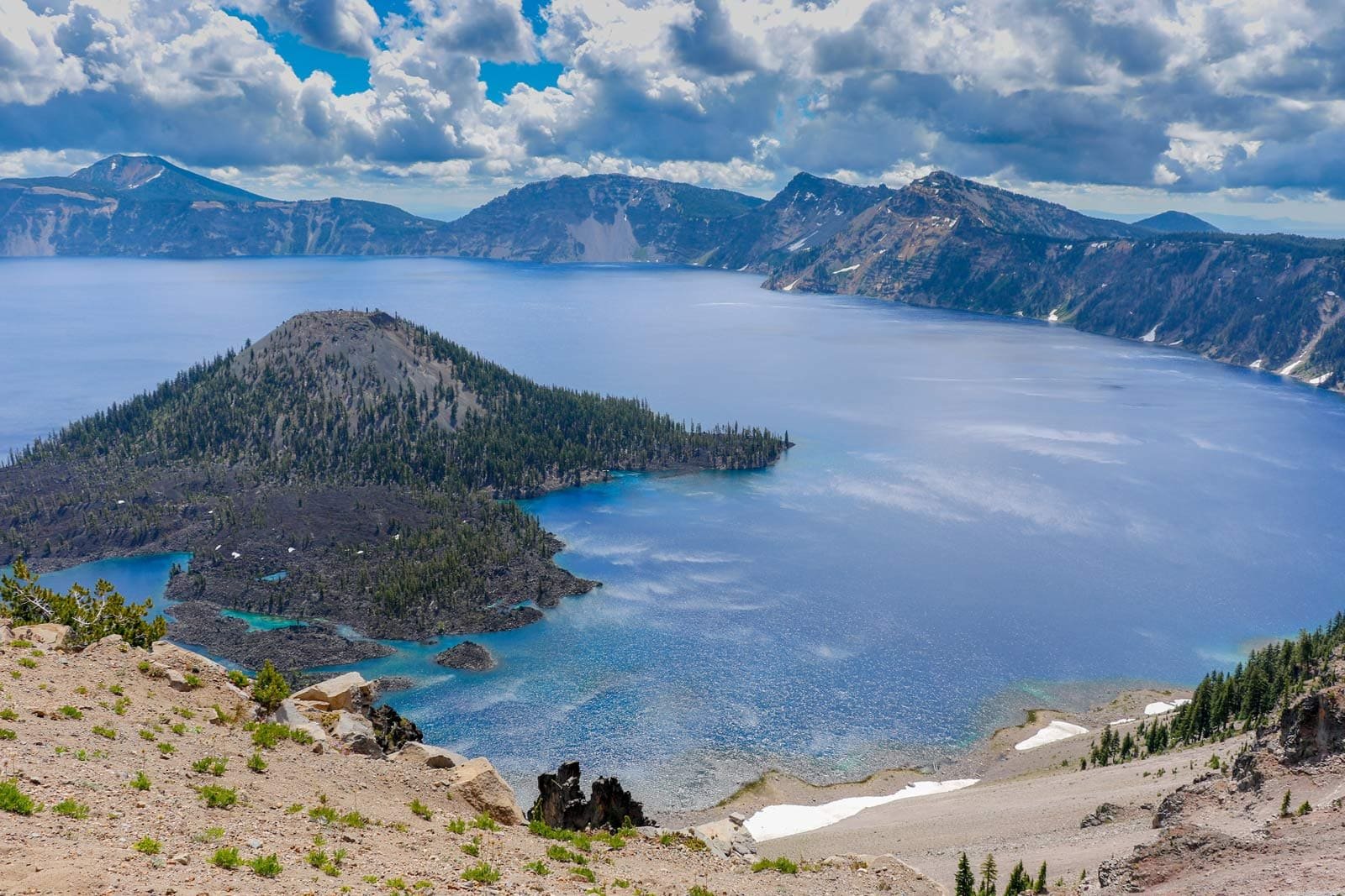 The deep, impossibly blue water of Crater Lake with Wizard Island in the center, one of the top US national parks.