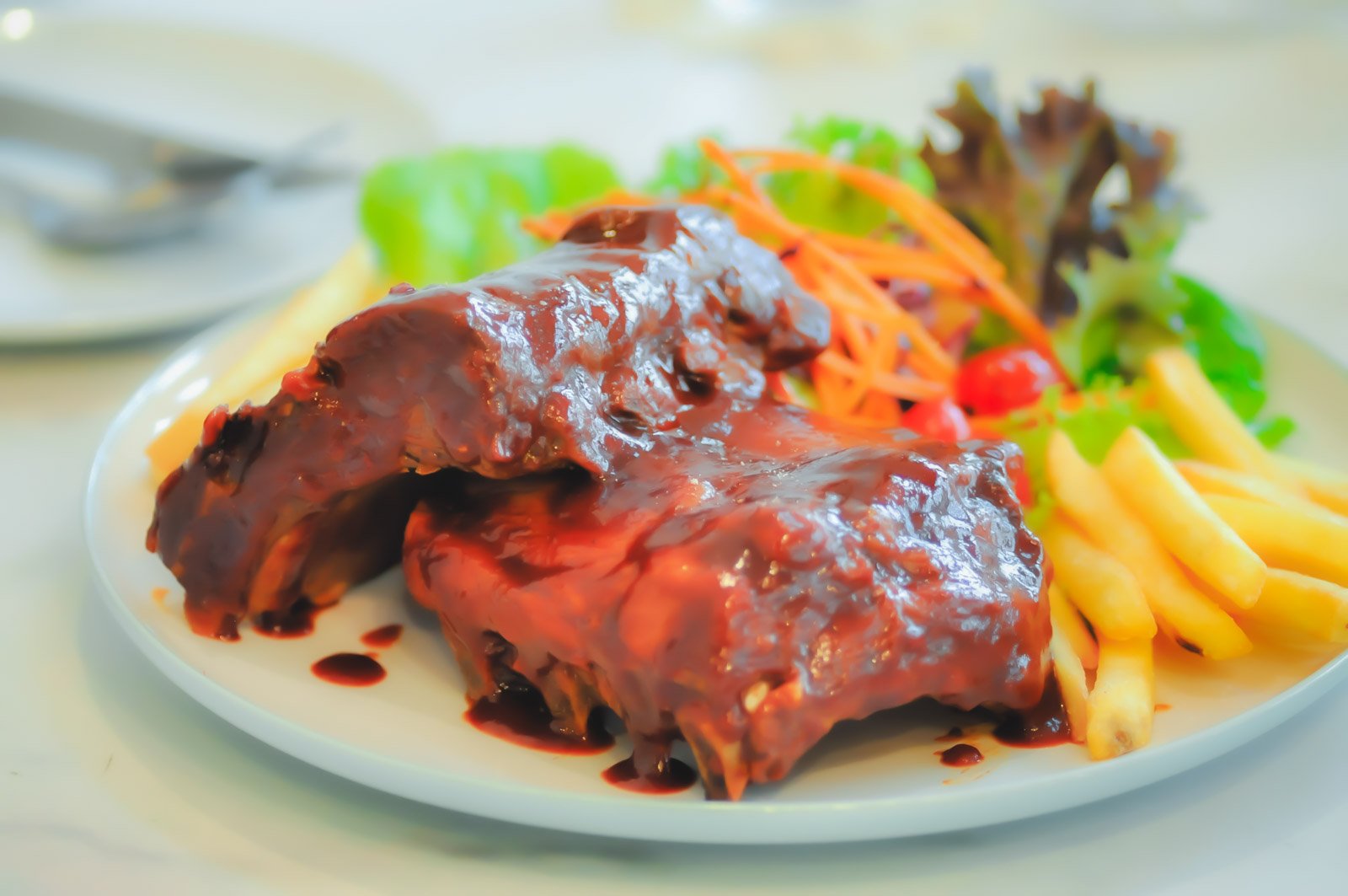A stack of sticky, guava-basted pork ribs with a glossy, dark red glaze on a white platter.