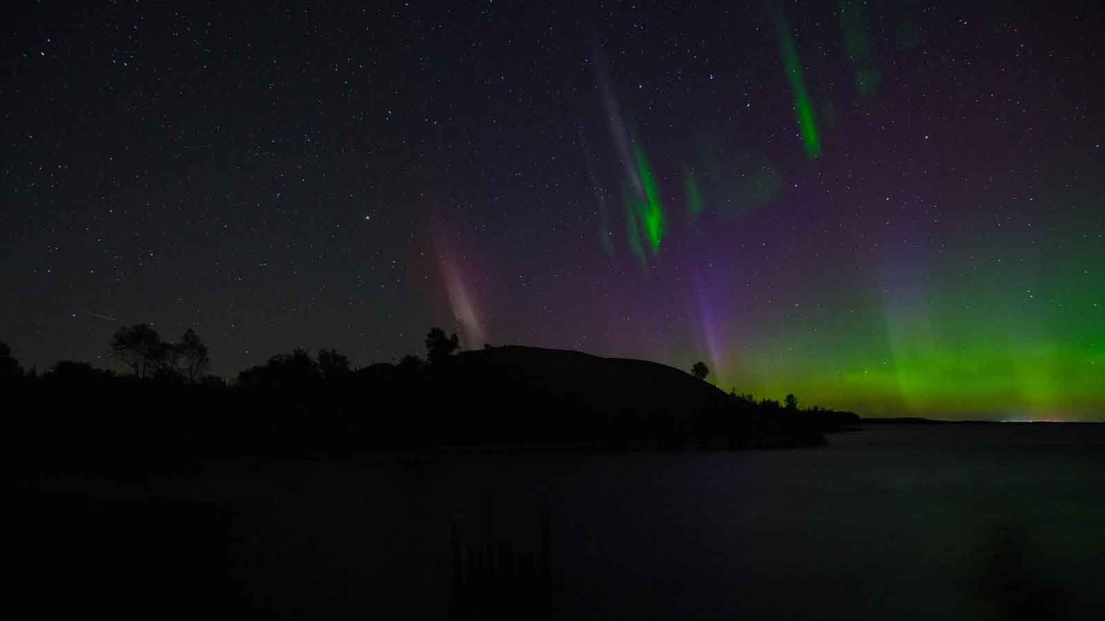 A vibrant aurora borealis, or Northern Lights, dancing in the dark sky over Lake Superior on the remote Keweenaw Peninsula