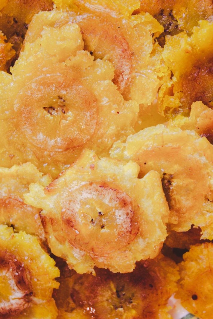A pile of golden-brown Tostones, which are double-fried and smashed green plantains, served with a garlic dipping sauce.