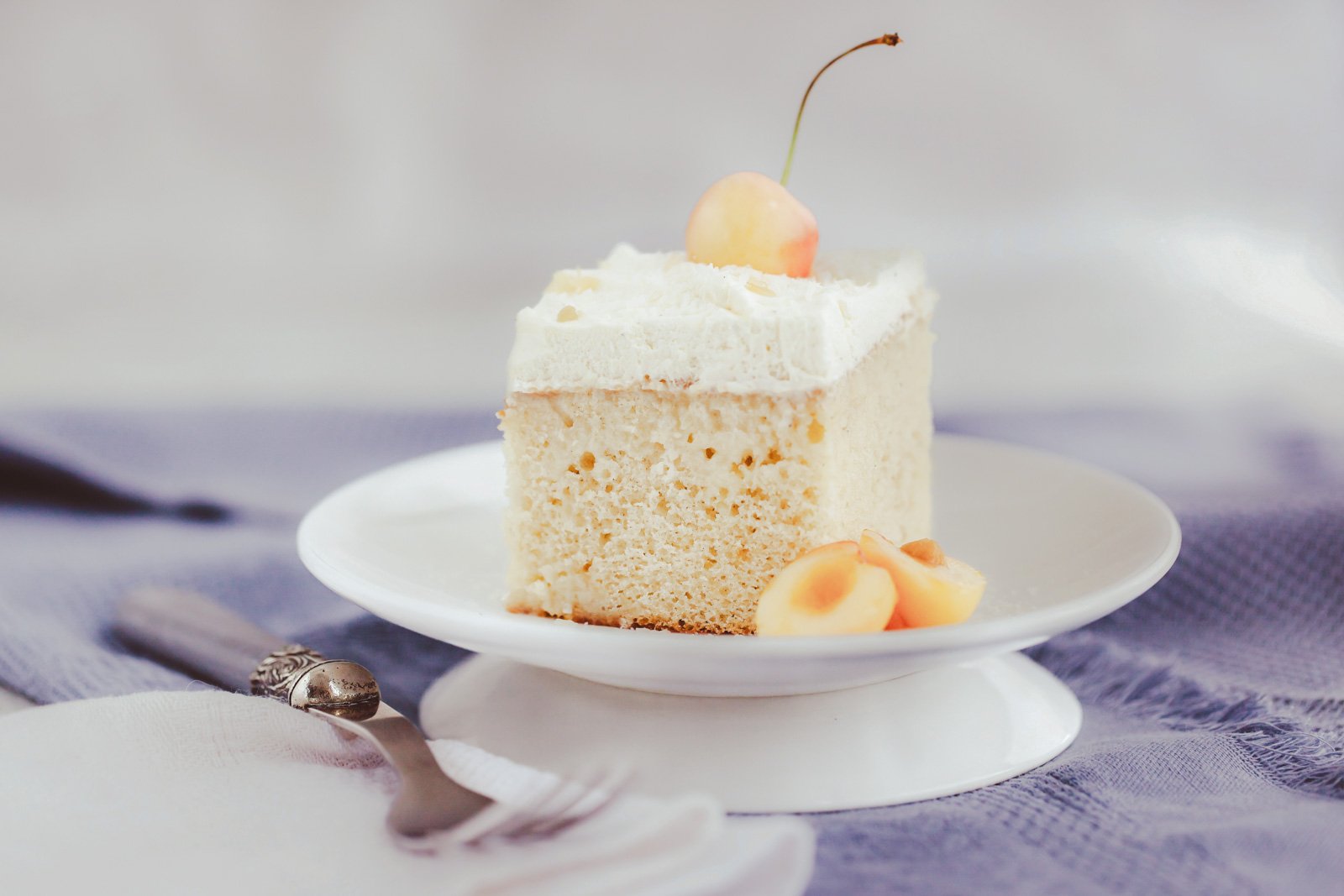 A slice of Tres Leches cake on a plate, with the three-milk mixture pooling at the bottom and a topping of whipped cream.