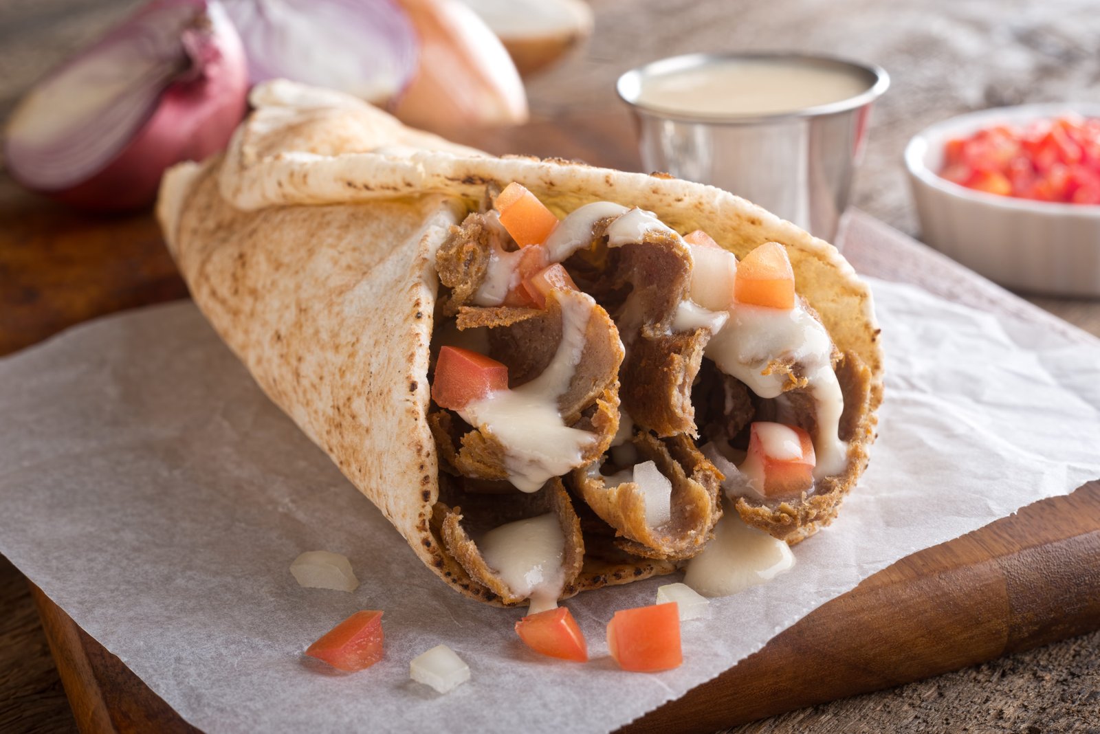 A close-up of a Halifax donair wrapped in foil, showing the meat and sweet donair sauce.