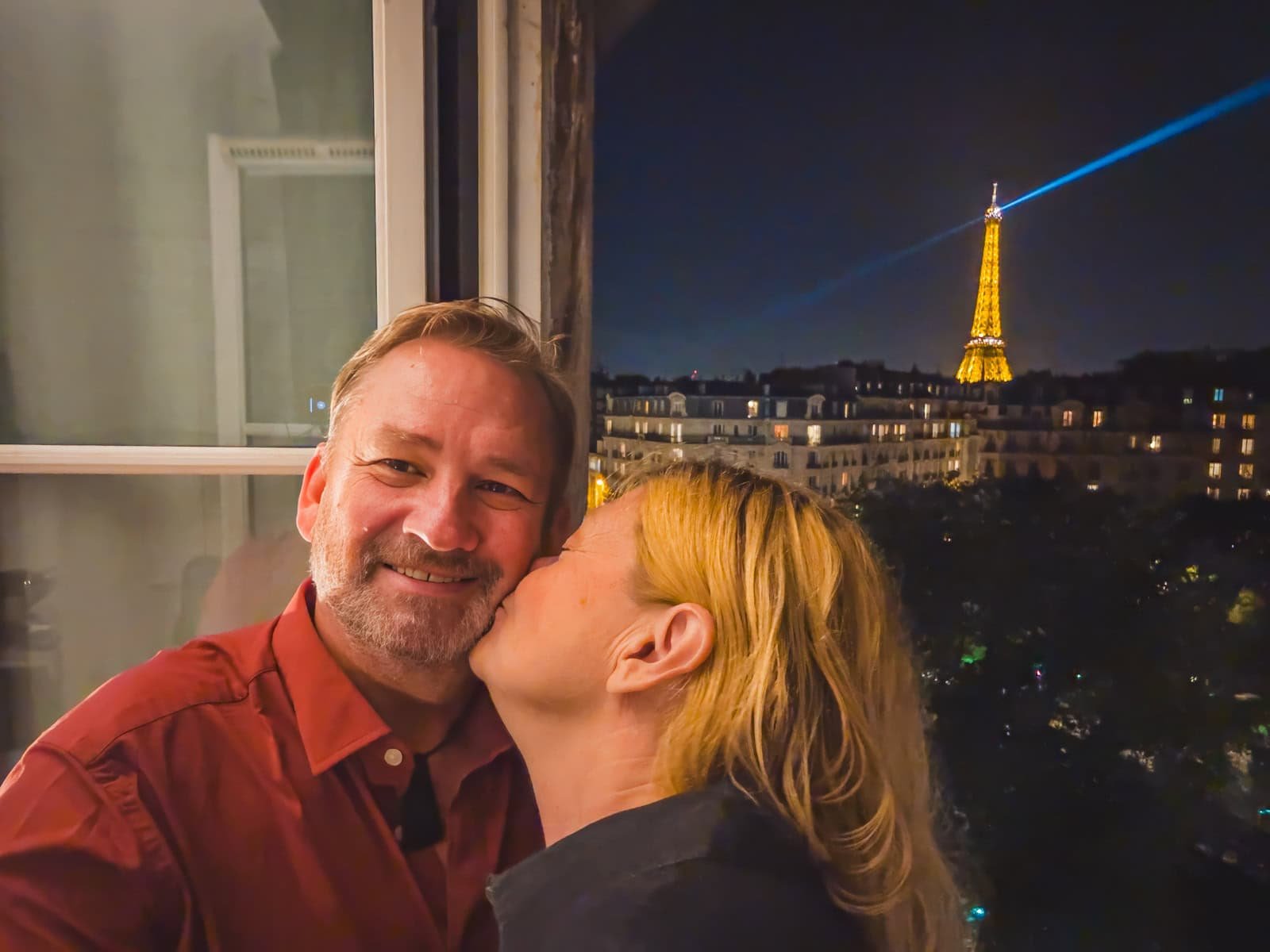 Deb from The Planet D snuggling on a Parisian balcony, overlooking the Eiffel Tower and the rooftops of the city at night.