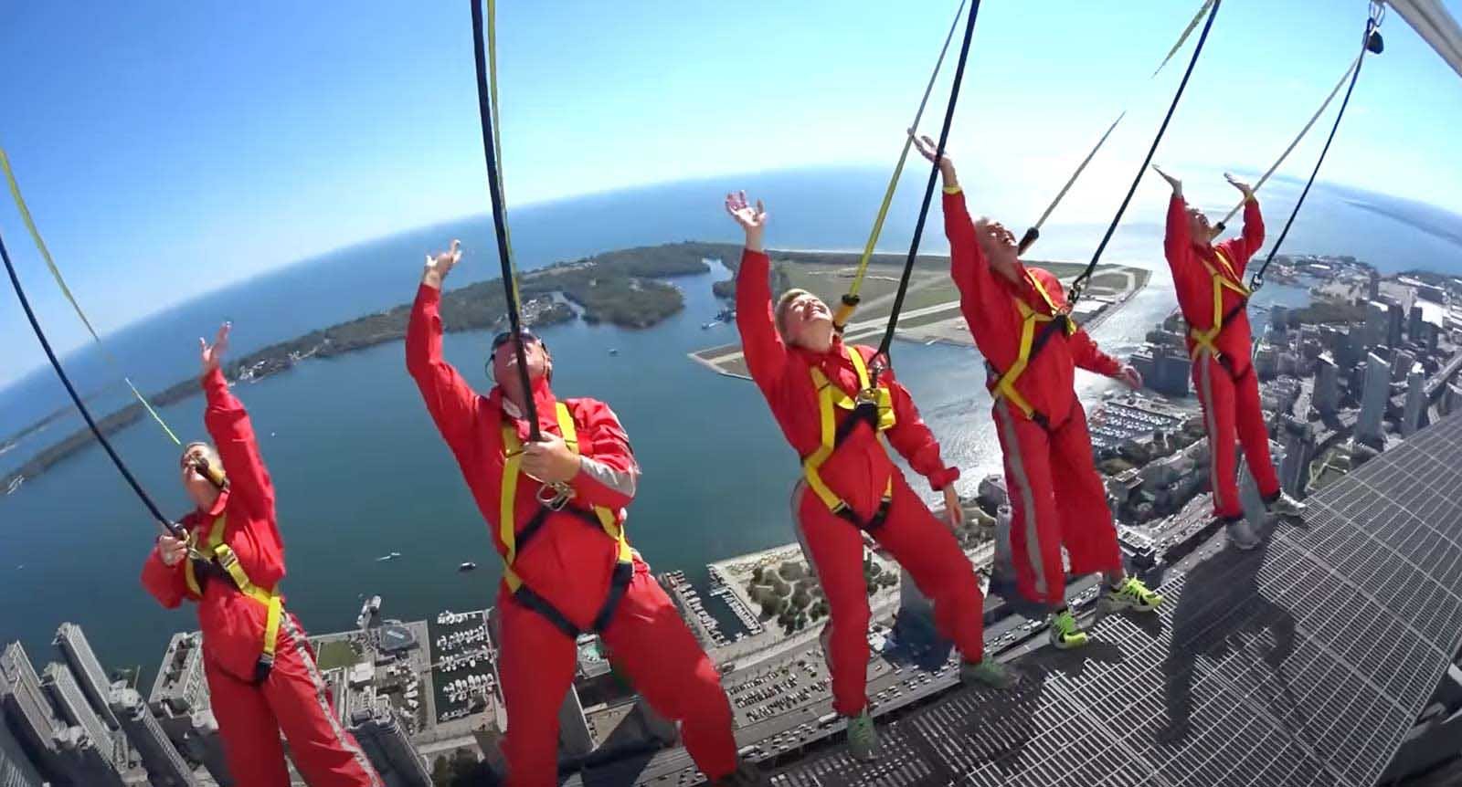 Dave and Deb's dad smiling and giving a thumbs-up in his orange jumpsuit while doing the CN Tower EdgeWalk high above Toronto.